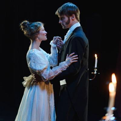Eine Opernsängerin und ein Opernsänger auf einer Bühne, elegant im Stil des Biedermeier gekleidet.