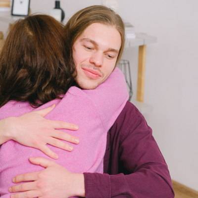 Ein junger Mann umarmt eine Frau mit lockigen Haaren und einem pinkfarbenen Pulli.