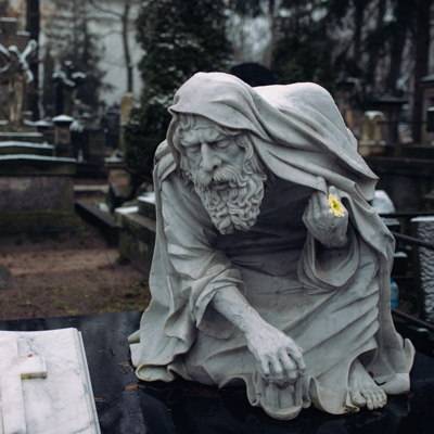 Marmorfigur eines alten Mannes auf einem Friedhof.
