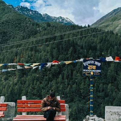Ein junger Mann mit einem Mobiltelefon sitzt vor der Bergkulisse des Himalaya.