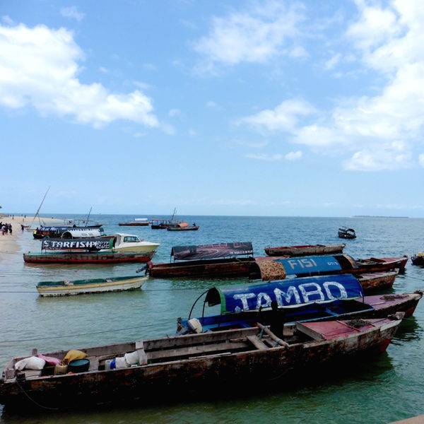 Fischerboote im Wasser vor einem Strand in Sansibar.